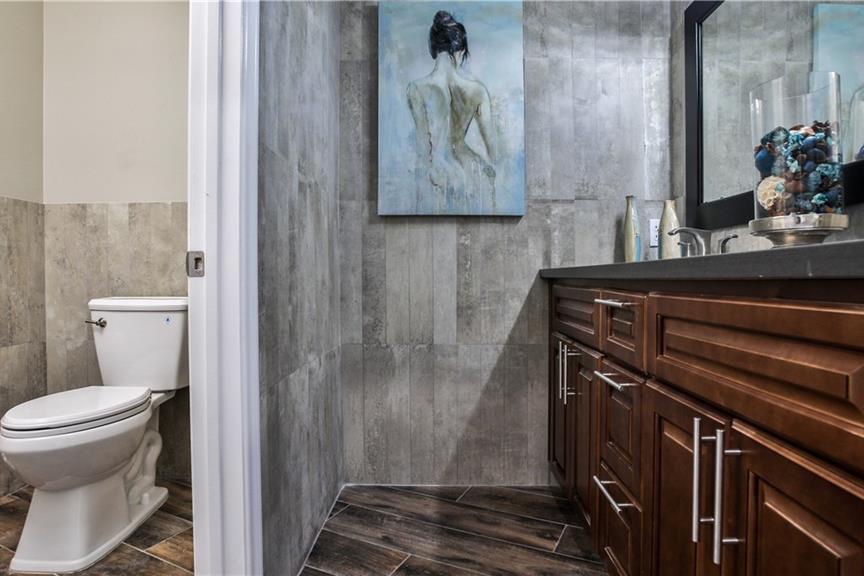 Remodeled bathroom with grey plank-tile walls, a dark wood vanity, a black stone counter, and a framed mirror