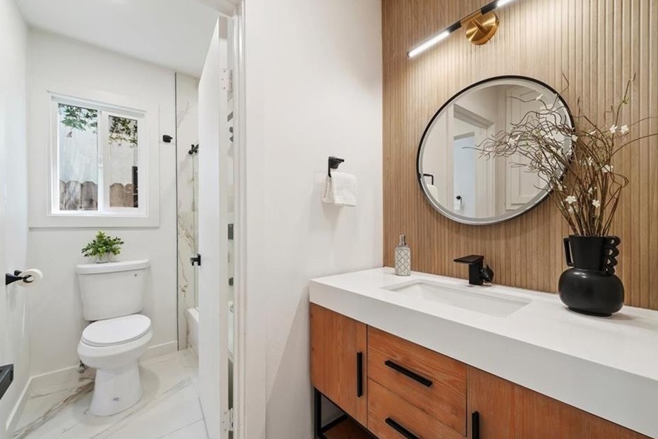 Remodeled bathroom with a wood-slat accent wall, a round mirror, a floating wood vanity, and black fixtures