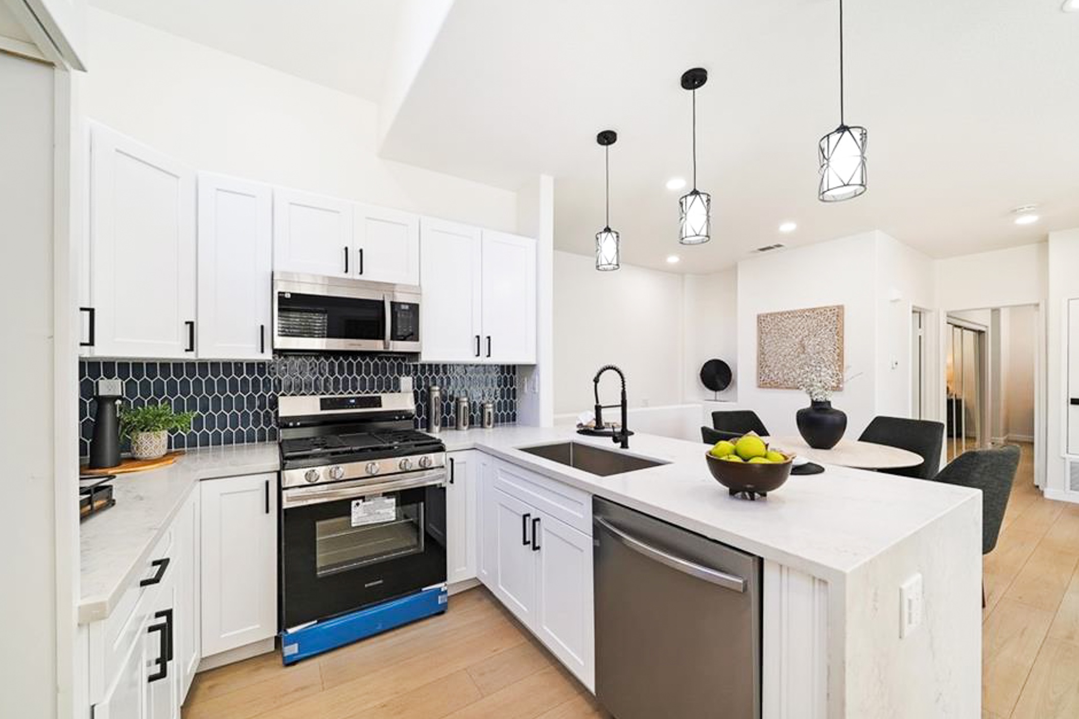 Remodeled kitchen with white shaker cabinetry, a navy picket-tile backsplash, stainless appliances, and a waterfall quartz peninsula